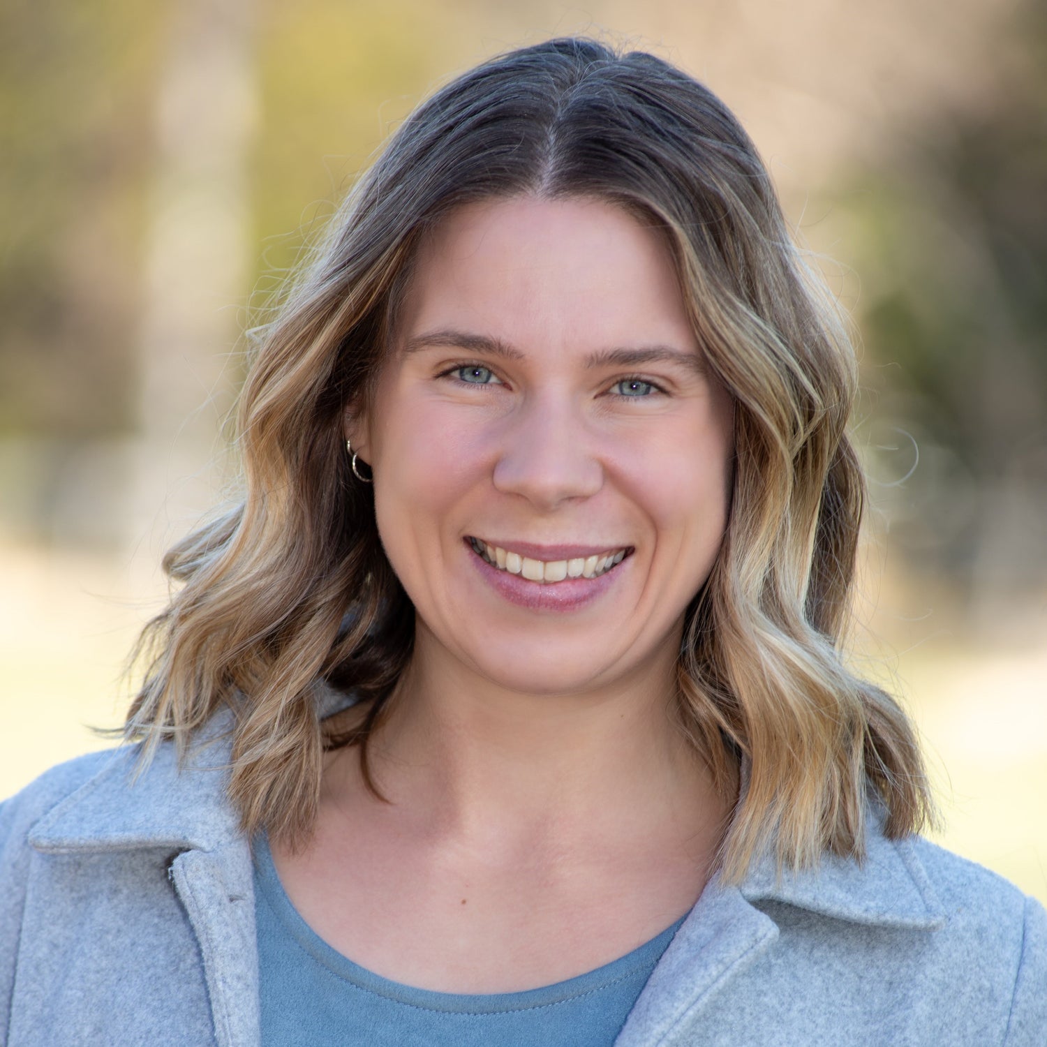Woman with blonde hair wearing a gray coat and blue shirt outdoors