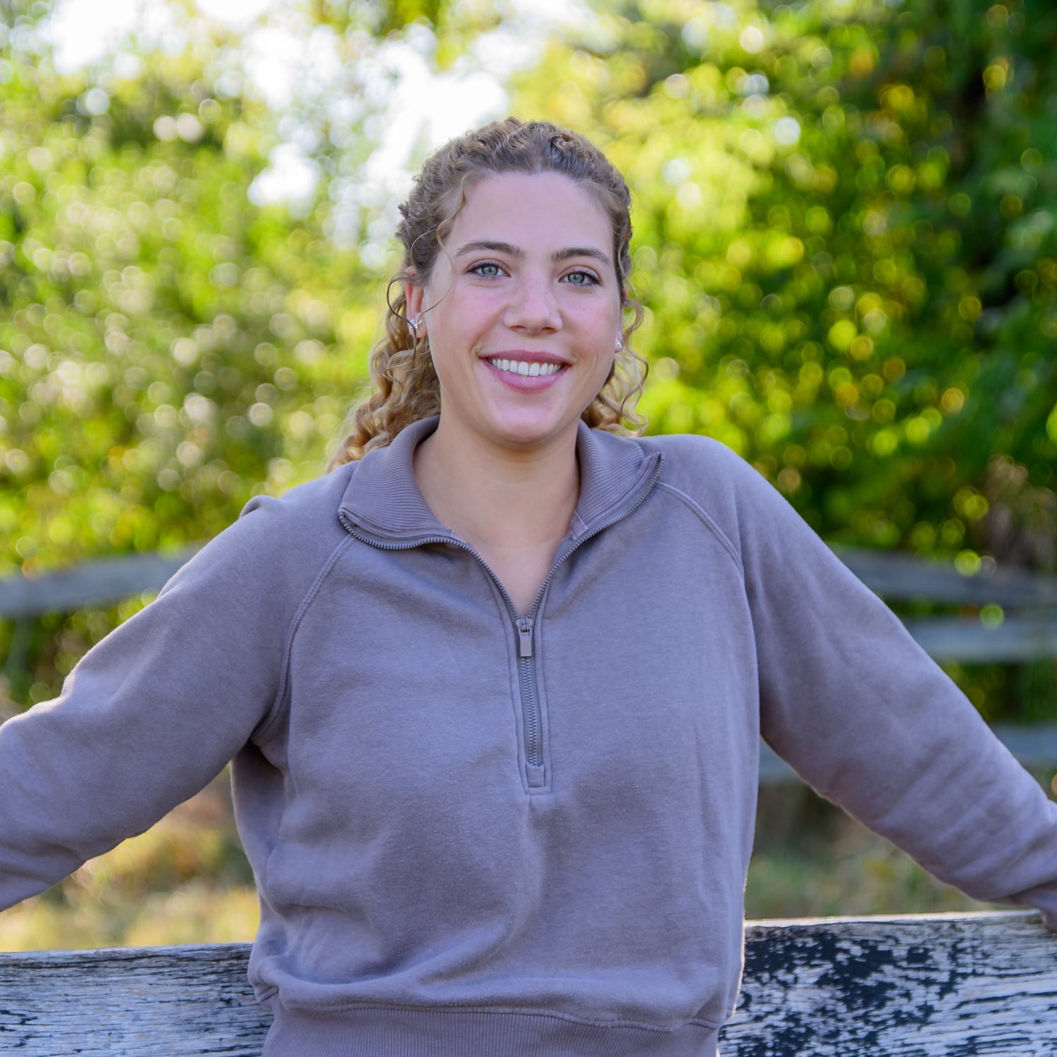 Woman standing by a wooden fence with trees in the background